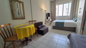 A room with a bed, a small table, a chair, a television, and a window. - Cozy in the heart of Leme (Rio de Janeiro)