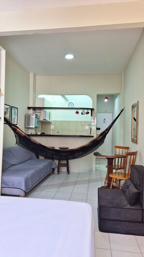 A room with a hammock, a bed, a sofa, a dining table with chairs, and a kitchen area in the background. - Cozy in the heart of Leme (Rio de Janeiro)