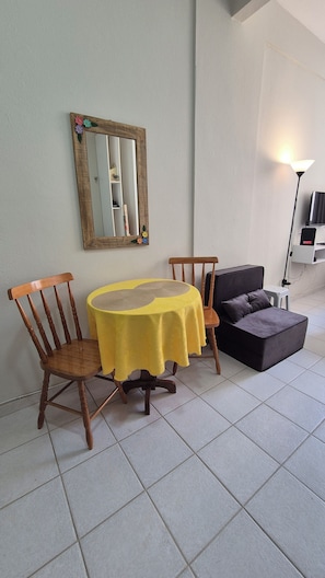 A dining area with a round table, two chairs, a sofa, a lamp, and a wall-mounted mirror. - Cozy in the heart of Leme (Rio de Janeiro)