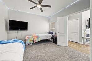 A bedroom with a ceiling fan, a flat-screen TV, a bed with a colorful blanket, a desk with a computer, and a door leading to another room. - Downtown Phoenix Retreat - Skyline Views + Pool (Phoenix)