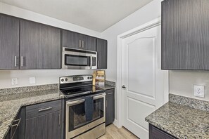 A compact kitchen with dark wood cabinets, a stainless steel microwave, a stove, and granite countertops. - Downtown Phoenix Retreat - Skyline Views + Pool (Phoenix)