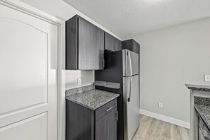 A kitchen with dark cabinetry, a stainless steel refrigerator, and a granite countertop. - Downtown Phoenix Retreat - Skyline Views + Pool (Phoenix)