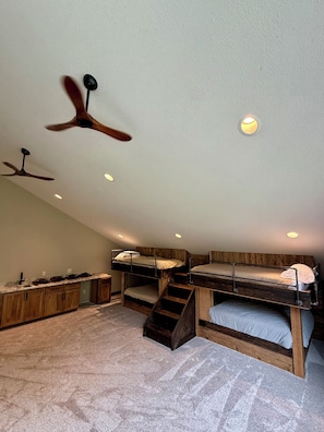 Ein Zimmer mit Etagenbetten, Holzschränken, einer Küchenzeile und Deckenventilatoren.