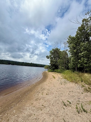 Eine natürliche Landschaft mit einem See, einem Sandstrand und einem bewaldeten Gebiet.