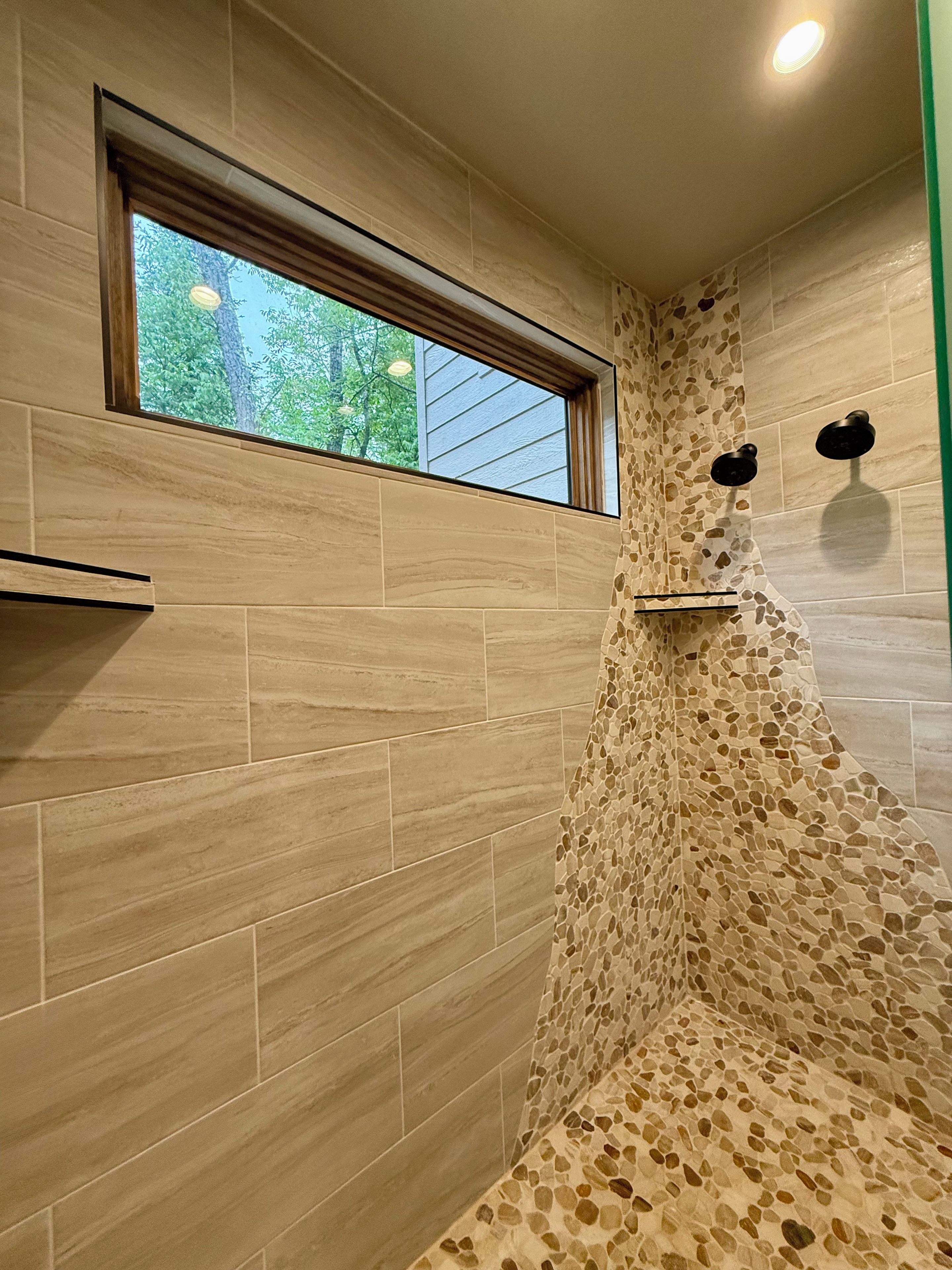 A shower area with a window, tiled walls, and a ceiling light.