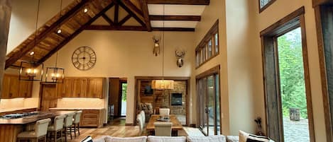 A spacious living area with a large sectional sofa, a wooden ceiling with exposed beams, and a circular light fixture.