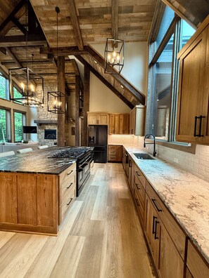 Une cuisine spacieuse dotée d’un grand îlot central, de meubles de rangement en bois et d’une cheminée en pierre.