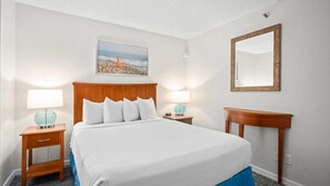 A hotel room with a bed, two bedside tables with lamps, a nightstand, a mirror, and a painting on the wall. - Ocean front condo in beautiful Ormond Beach at Tropic Sun Towers (Ormond Beach)