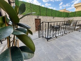 Un patio con cerca de hierro forjado, mobiliario exterior y un muro de seto verde.