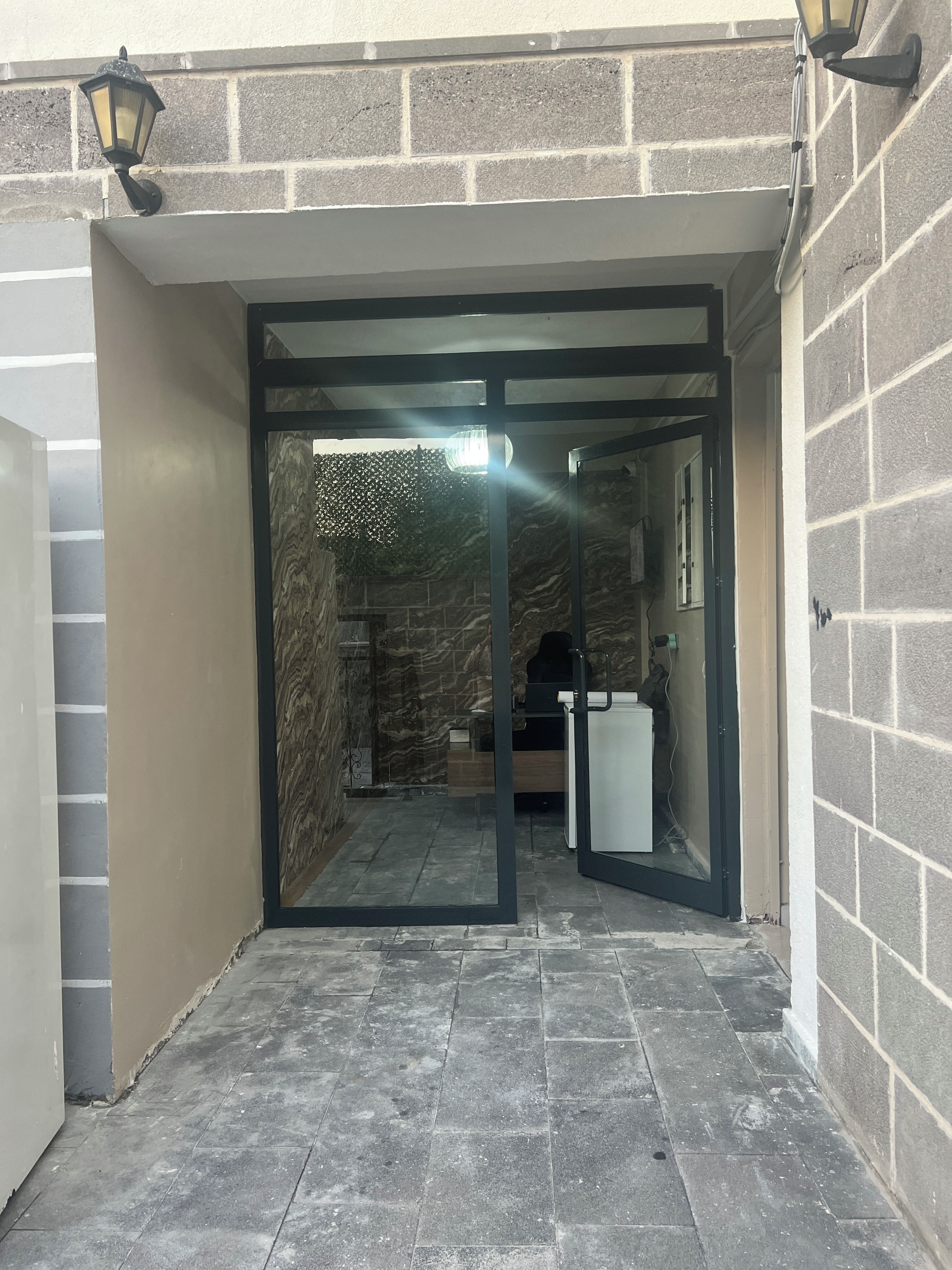 A building entrance with a glass door, a stone wall, and a tiled floor.