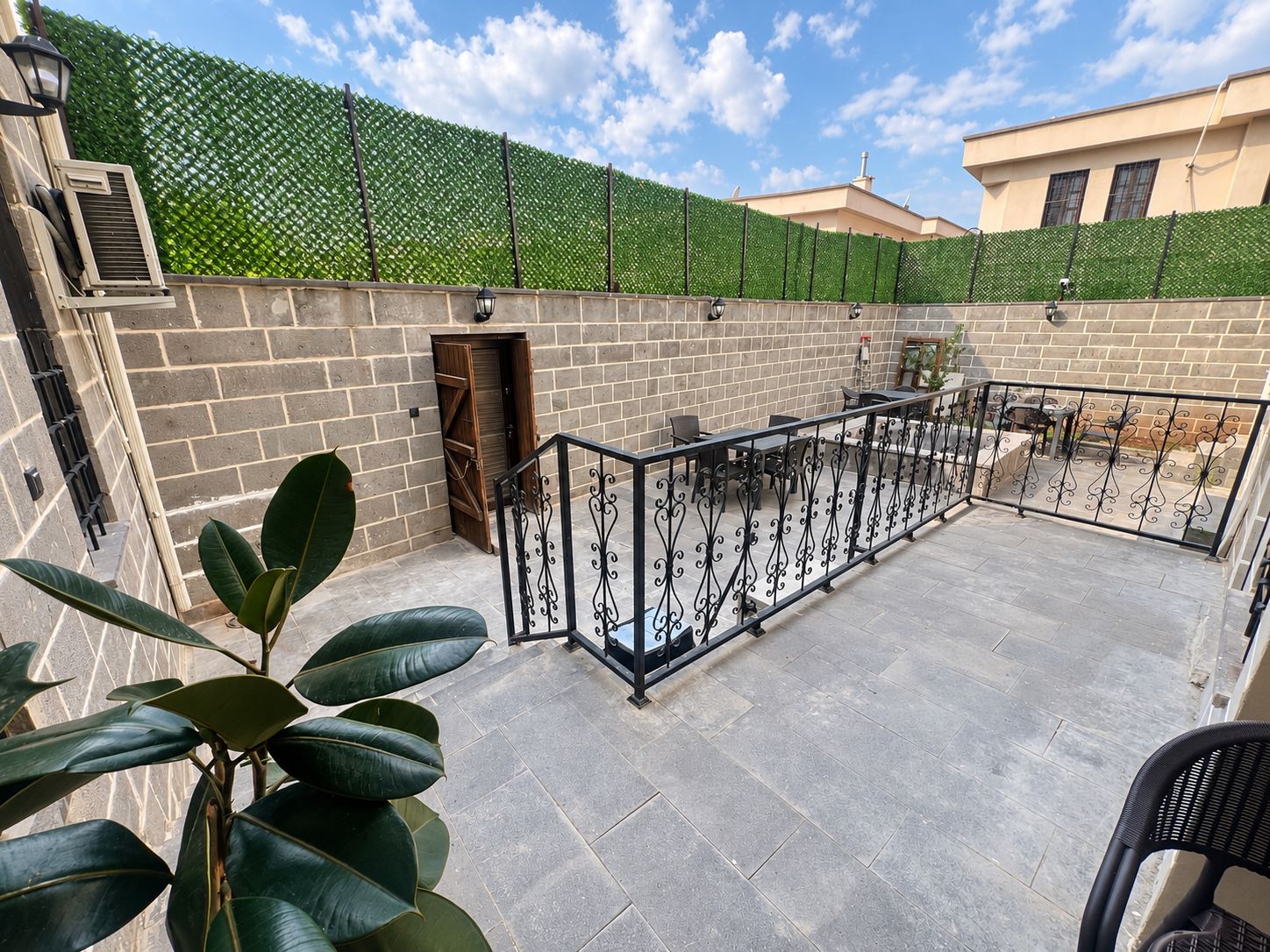 Une terrasse sur le toit, avec un mur en briques, une rambarde en métal et une haie verdoyante.