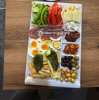 Un plato rectangular con diversos alimentos, como verduras en rodajas, queso, huevos, aceitunas y garbanzos.