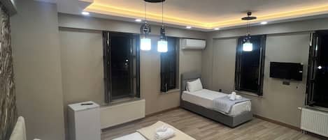 Egy modern szállodaszoba, amelyben egy nagy ágy, egy éjjeliszemélyzet, egy falra szerelt, síkképernyős televízió és egy kilátással rendelkező ablak található.