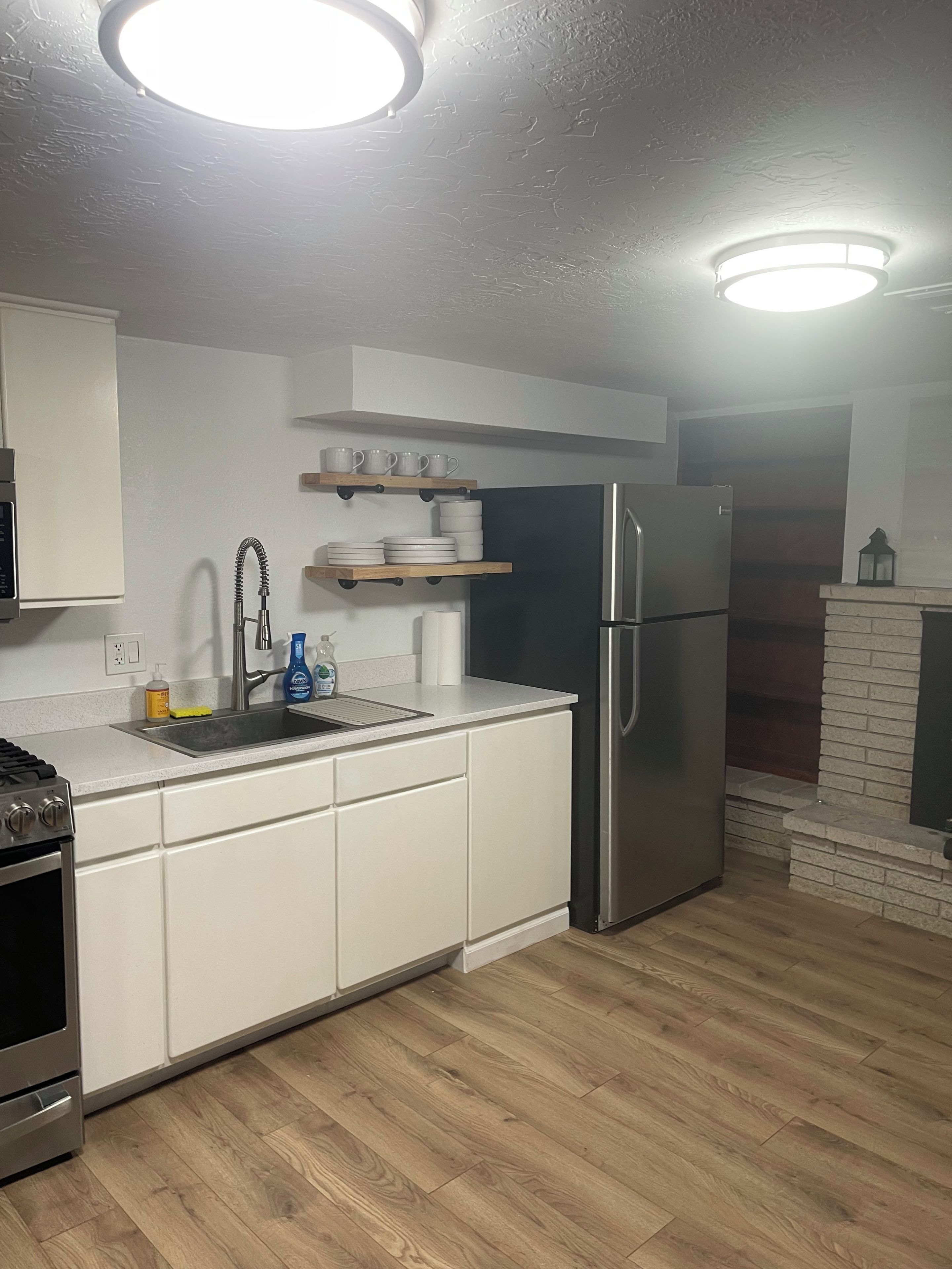 A modern kitchen with white cabinets, a stainless steel refrigerator, a built-in oven, and a wooden floor.