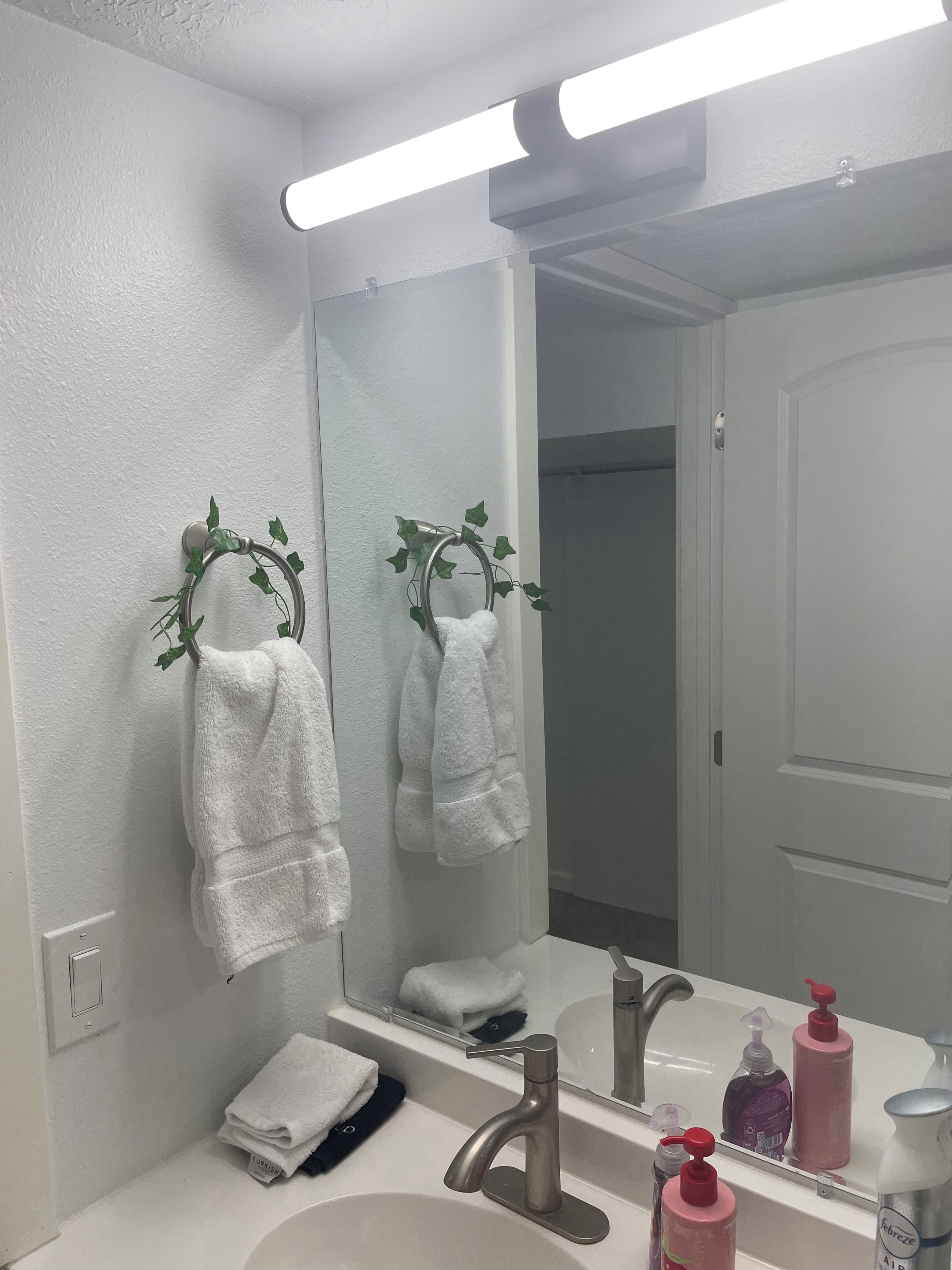 Un bagno con un lavandino bianco, uno specchio e un portascopino con un asciugamano bianco.