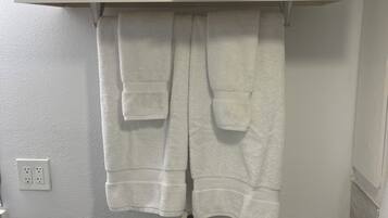 A bathroom with a toilet, a towel rack with two towels, and a roll of toilet paper.