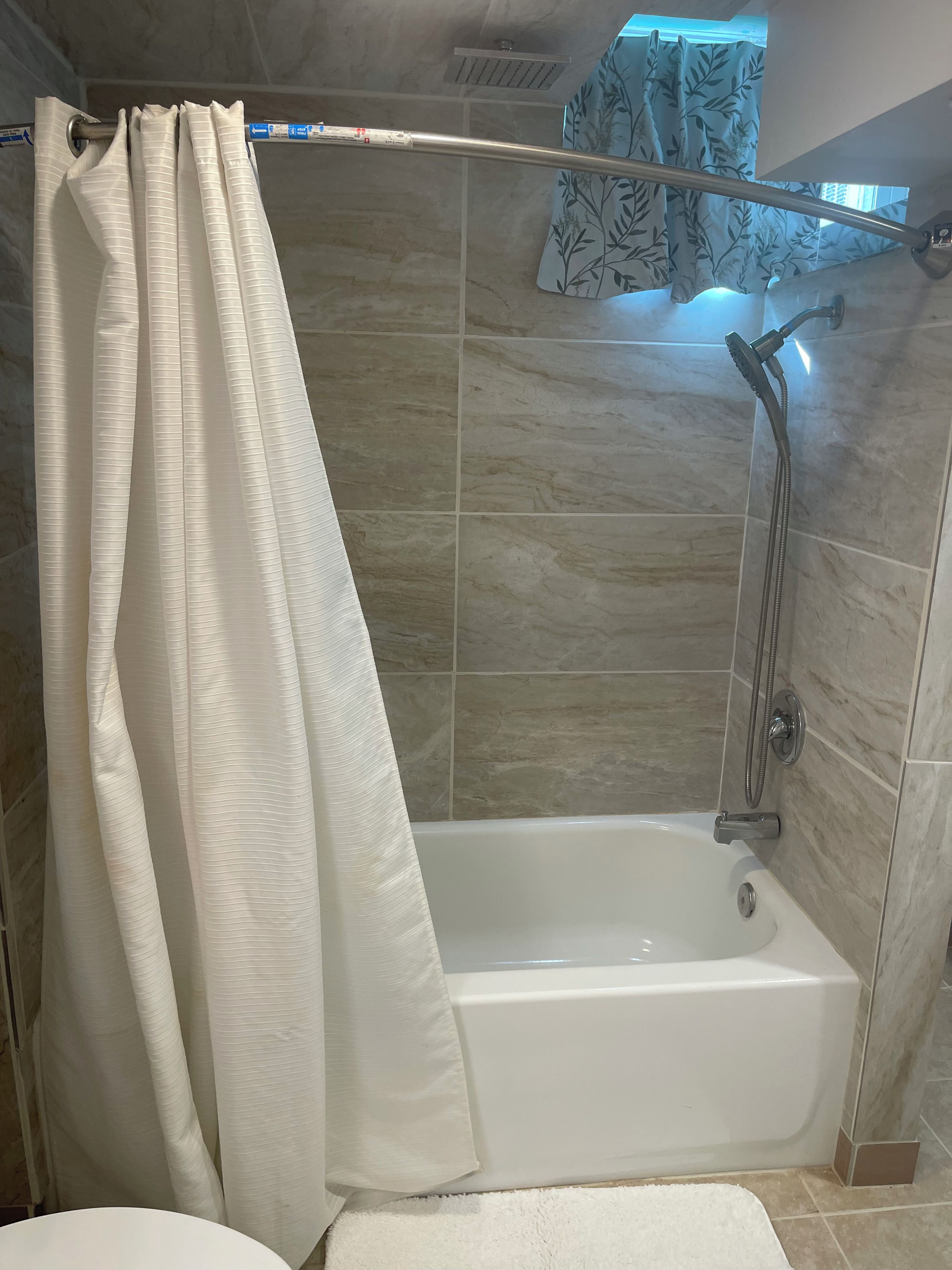 A shower area with a glass door, a white bathtub, and a showerhead.