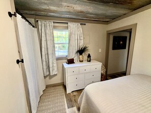 A bedroom with a bed, a dresser, a window with curtains, and a door.