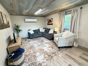 A living room with a sectional sofa, a patterned rug, a side table with a lamp, and a large window with curtains. - Serene 1-bedroom tiny house in charming Strawberry, steps away from the creek (Strawberry)