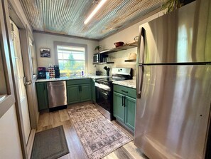 A kitchen with green cabinets, stainless steel appliances, a microwave, and a refrigerator.