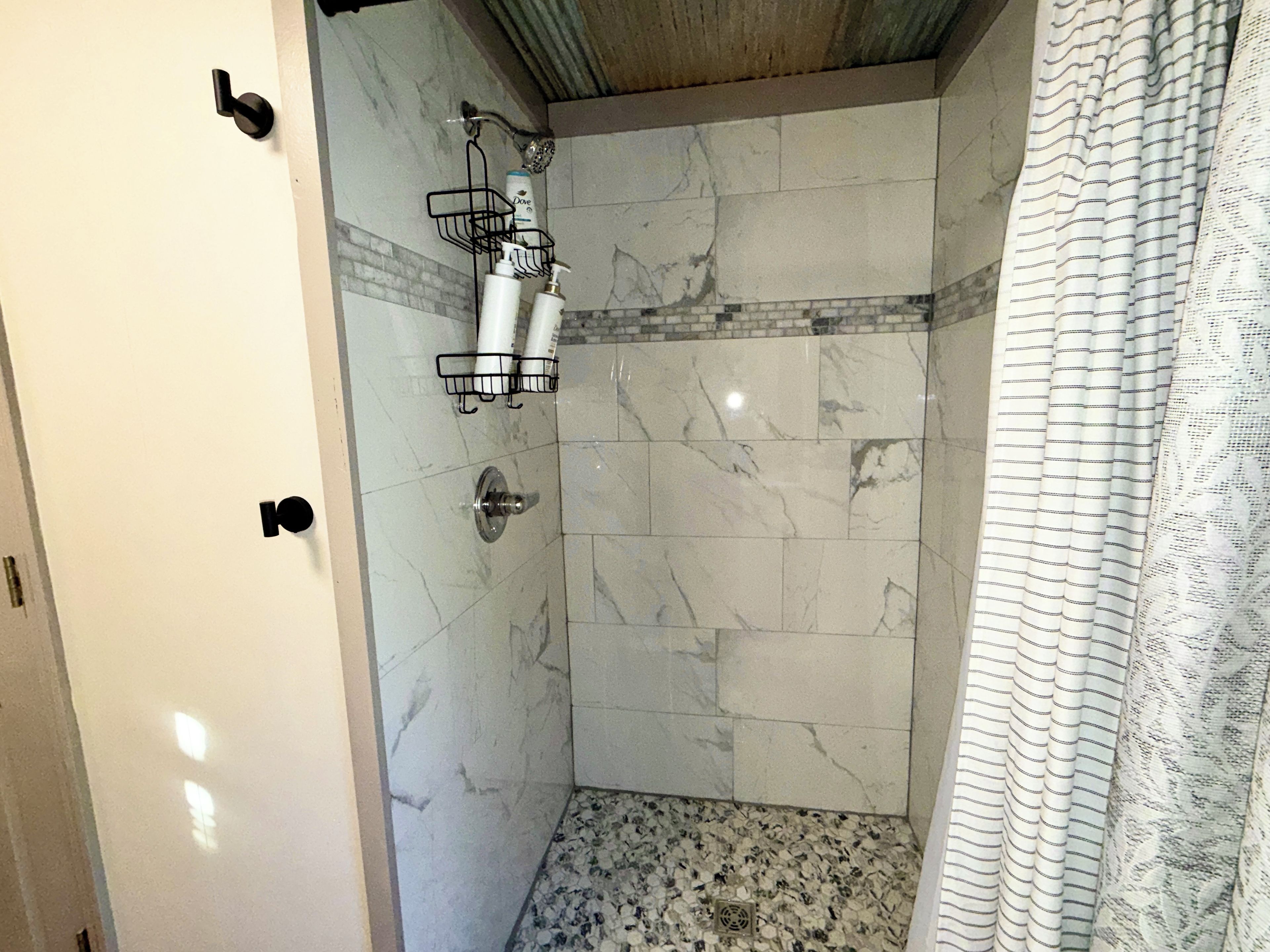 A bathroom with a shower, marble tiles, a towel rack, and a shower curtain.