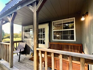 A wooden porch with a bench, a welcome sign, and a window with a view of trees. - Serene 1-bedroom tiny house in charming Strawberry, steps away from the creek (Strawberry)