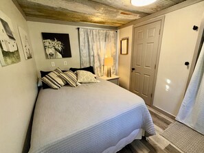 Ein Schlafzimmer mit einem Bett, einem Nachttisch, einer Lampe, einer Tür und einer Wand mit gerahmten Bildern.