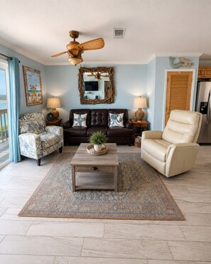 A living room with a sofa, armchair, coffee table, and a ceiling fan. - Bayfront Retreat for Two - Pool + Gulf Nearby (Fort Walton Beach)