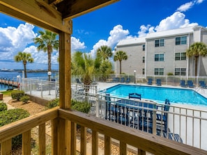 A pool area with a view of the ocean, a wooden deck, and a building with multiple windows. - Bayfront Retreat for Two - Pool + Gulf Nearby (Fort Walton Beach)