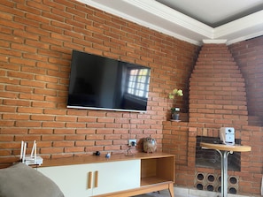 Una habitación con pared de ladrillo, un televisor de pantalla plana montado sobre un mueble de madera, una mesita con un altavoz y un adorno decorativo de búho.