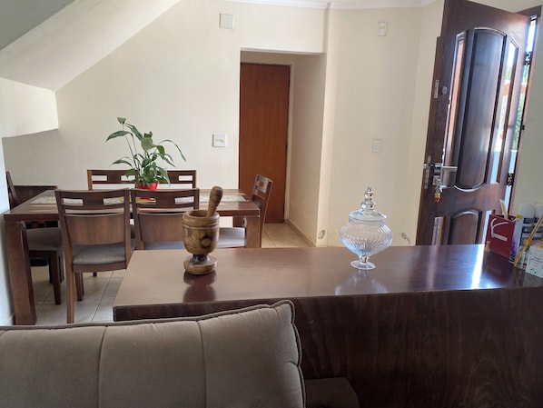 Un comedor con una mesa de madera, sillas, una planta en maceta y un tarro de vidrio sobre la mesa.