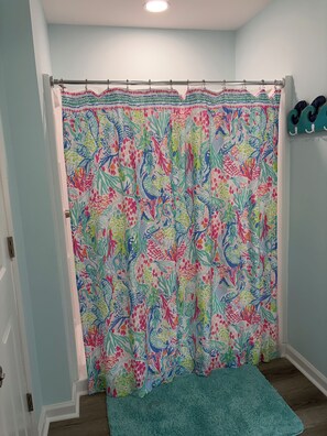 A bathroom with a shower curtain featuring a floral pattern, a blue bath mat, and a towel rack with towels. - Peaceful 3-bedroom house with a Heated Pool! (Oak Island)