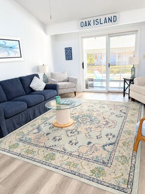 Een moderne woonkamer met een blauwe bank, een kamerkleed met patroon en een glazen salontafel.