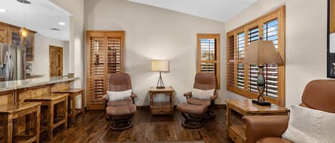 A spacious living room with a wooden floor, leather chairs, a sofa, a dining area with a wooden table, and a kitchen with wooden cabinets.