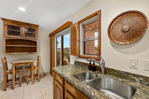 A kitchen with wooden cabinets, a granite countertop, a stainless steel sink, and a window with wooden shutters. - The Hilltop Lookout | Catalina Mountain Views (Tucson)