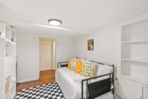 A bedroom with a bed, a checkered rug, a wardrobe, and a door leading to another room.