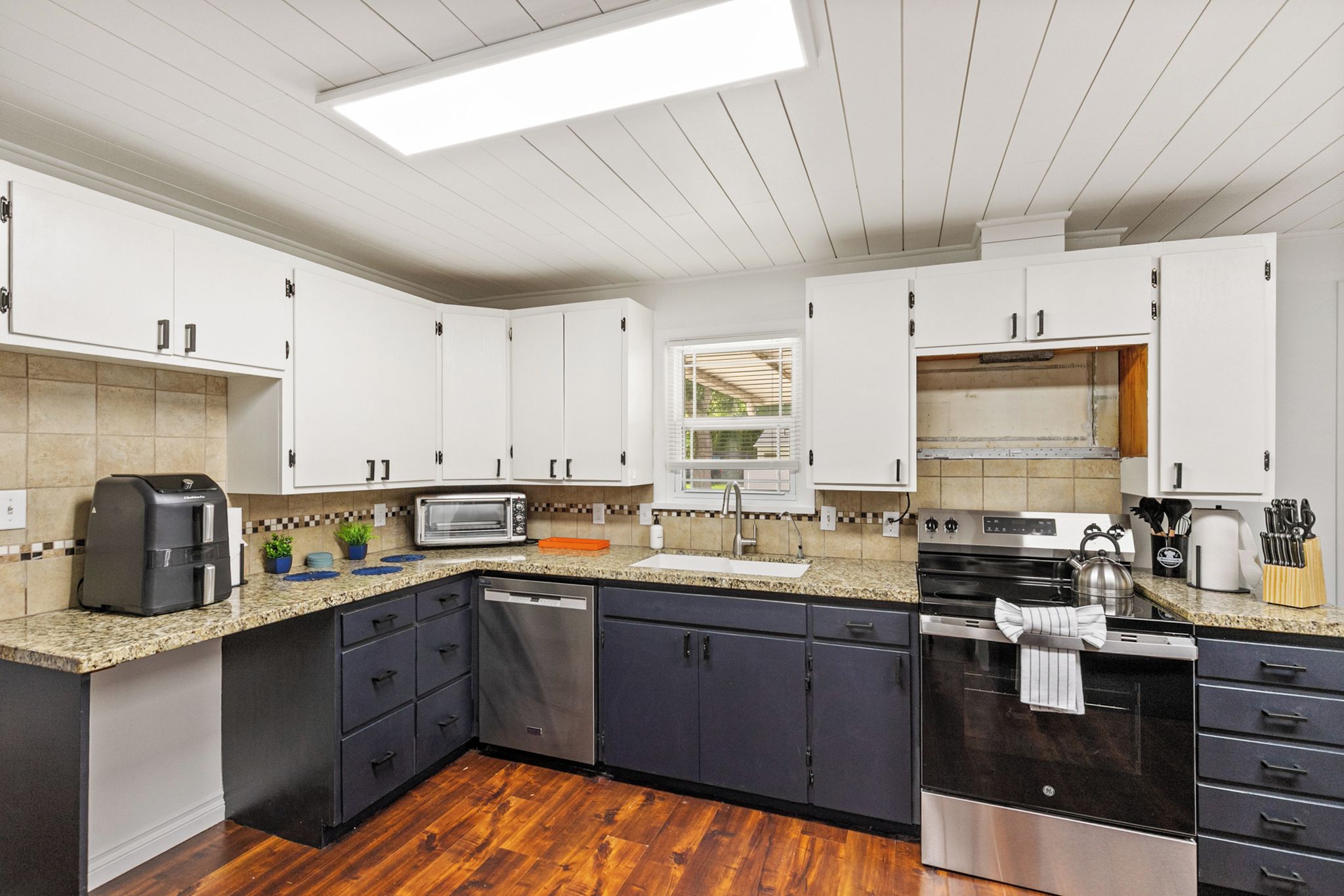 A modern kitchen with white cabinets, a built-in oven, a dishwasher, and a granite countertop.