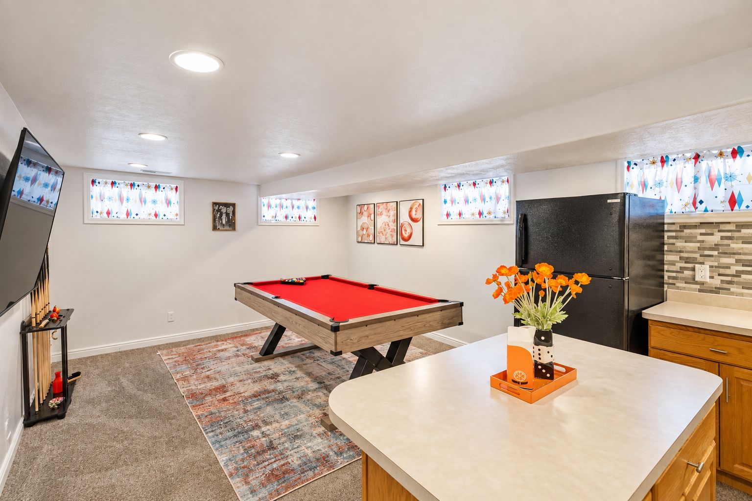 Una mesa de billar en una habitación con zona de cocina, un refrigerador y un televisor.