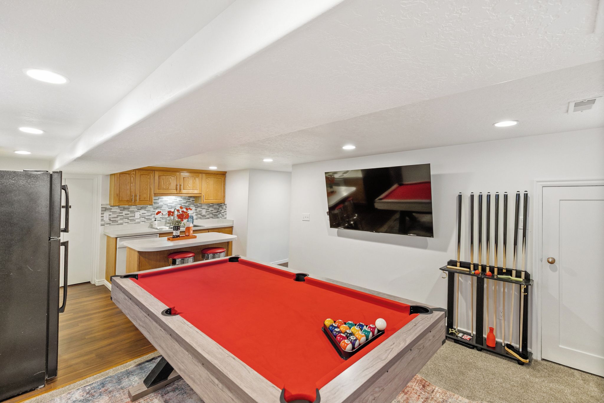 A compact living space with a pool table, a kitchen area, and a billiards rack.