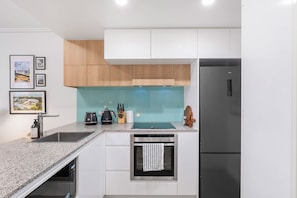 A modern kitchen with a built-in oven, a refrigerator, and a countertop with a toaster and a kettle. - Funky Teneriffe - 2Bed-2Bath-Balcony-1Car (Teneriffe)