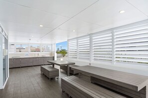 Eine saubere, moderne Küche mit weißen Schränken, einem Holztisch und Blick durch große Fenster.