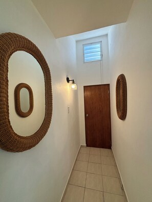 Een gang met een houten deur, een wandlamp en twee grote wandversieringen van geweven materiaal.