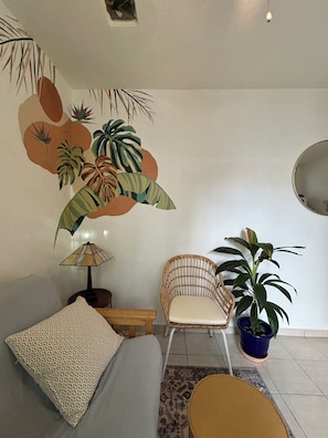 Een slaapkamer met een bed, een stoel, een lamp, een kamerplant en een muurschildering.