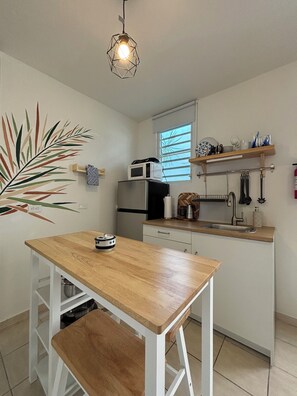 Een kleine keuken met een houten tafel, een magnetron en een spoelbak.