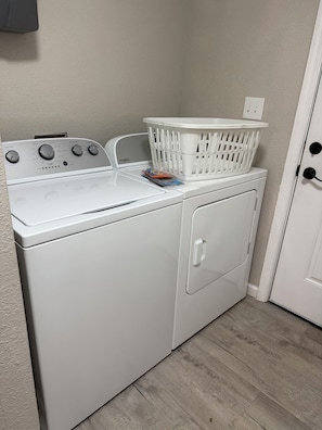 Een wasmachine en droger met voorlaadopening, een witte wasmand erbovenop, een tijdschrift op de droger en een wandcontactdoos.