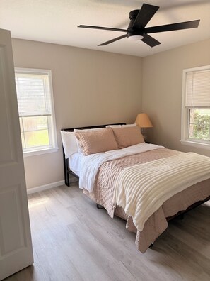 Ein Schlafzimmer mit einem Bett, einem Deckenventilator und zwei Fenstern mit Jalousien.