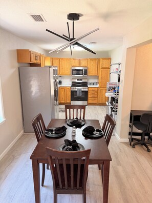 A modern kitchen with wooden cabinets, stainless steel appliances, and a dining table set for four. - Newly Renovated Tallahassee Retreat Minutes from FAMU, FSU & Downtown (Tallahassee)