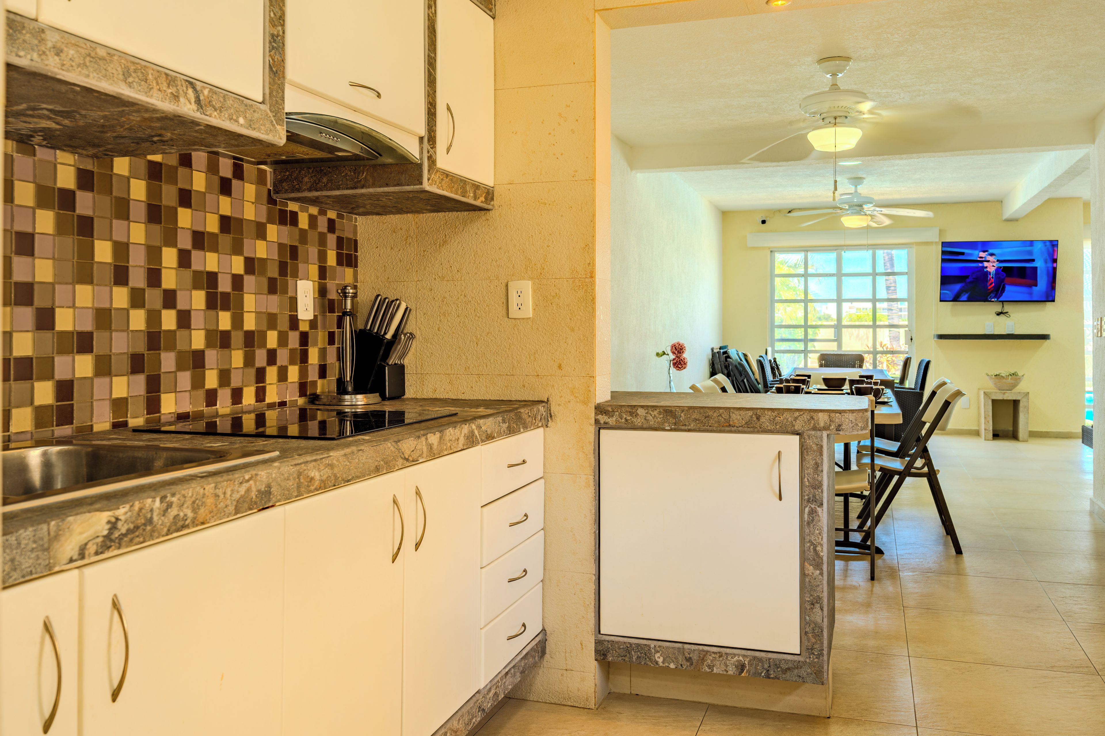 A kitchen with a checkered backsplash, a dining area with a TV, and a ceiling fan.
