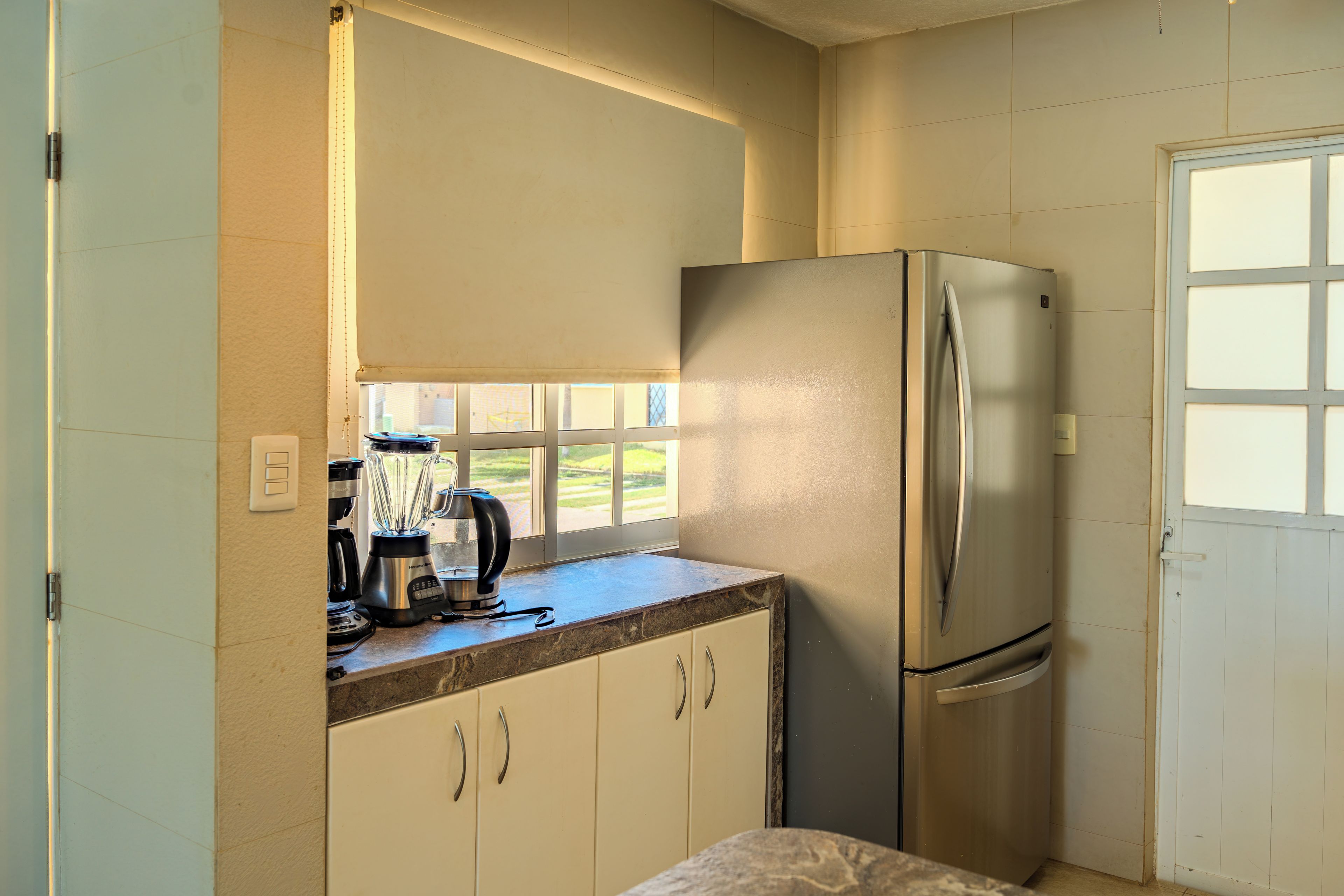 Cocina compacta con refrigerador, cafetera y ventana con vistas a un paisaje verde.