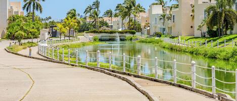 A waterfront promenade with a curved walkway, a small water feature, and palm trees.